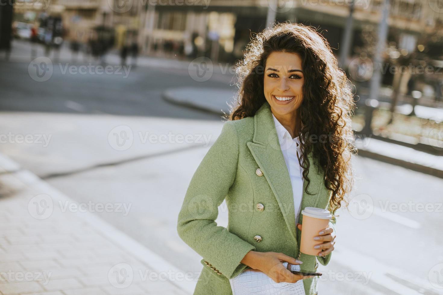 jovem mulher usando smartphone na rua e segurando café para viagem foto