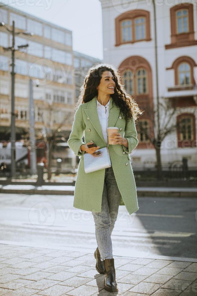 jovem mulher usando smartphone na rua e segurando café para viagem foto