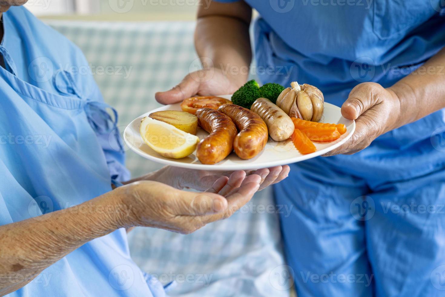 paciente idosa asiática ou idosa tomando café da manhã e comida saudável vegetal com esperança e feliz enquanto está sentado e com fome na cama no hospital. foto
