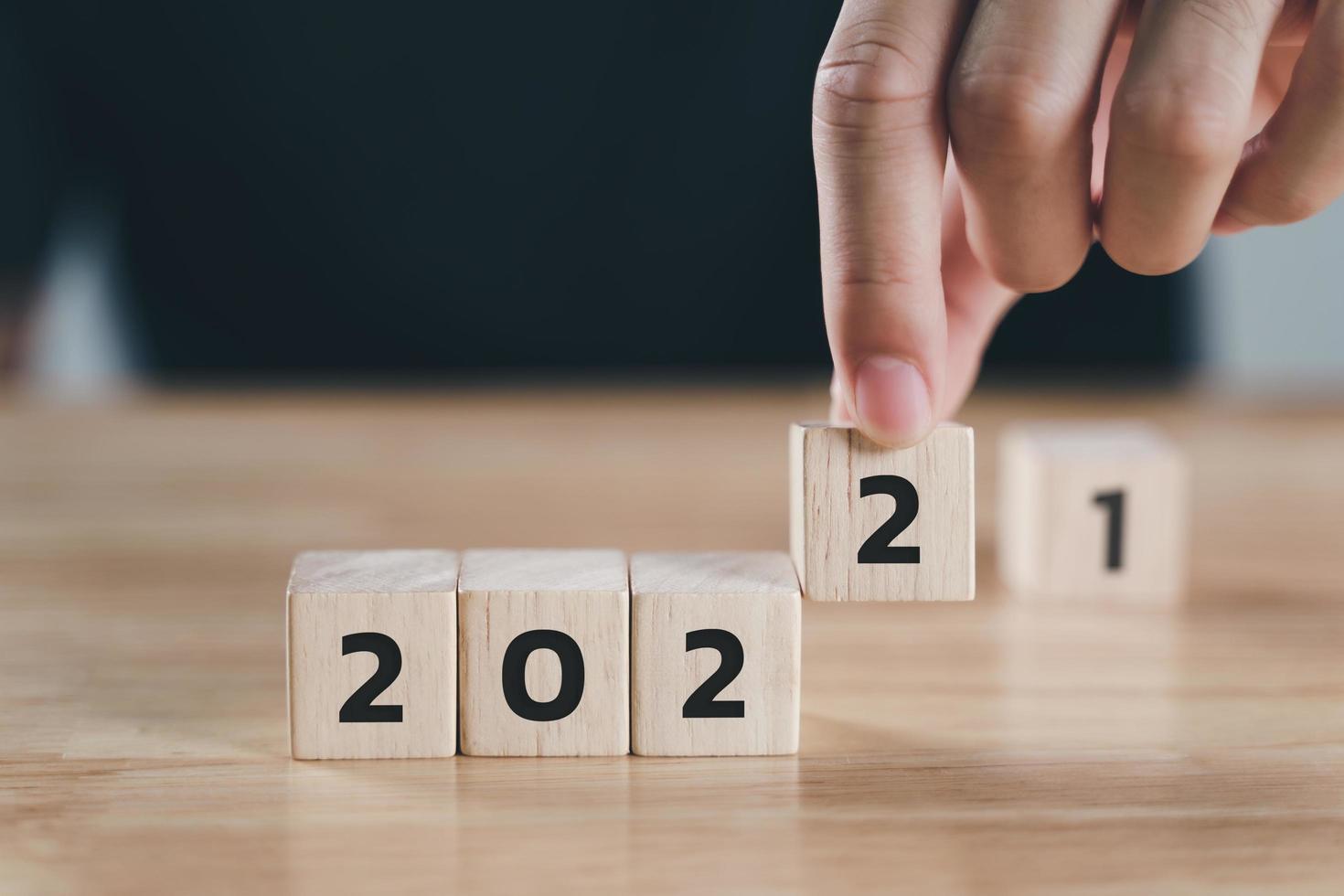 mão do homem colocando bloco de cubo de madeira para alterar o ano de 2.021 a 2.022 anos na mesa de madeira com espaço de cópia. início ao ano de 2022. conceito de feliz ano novo. foto