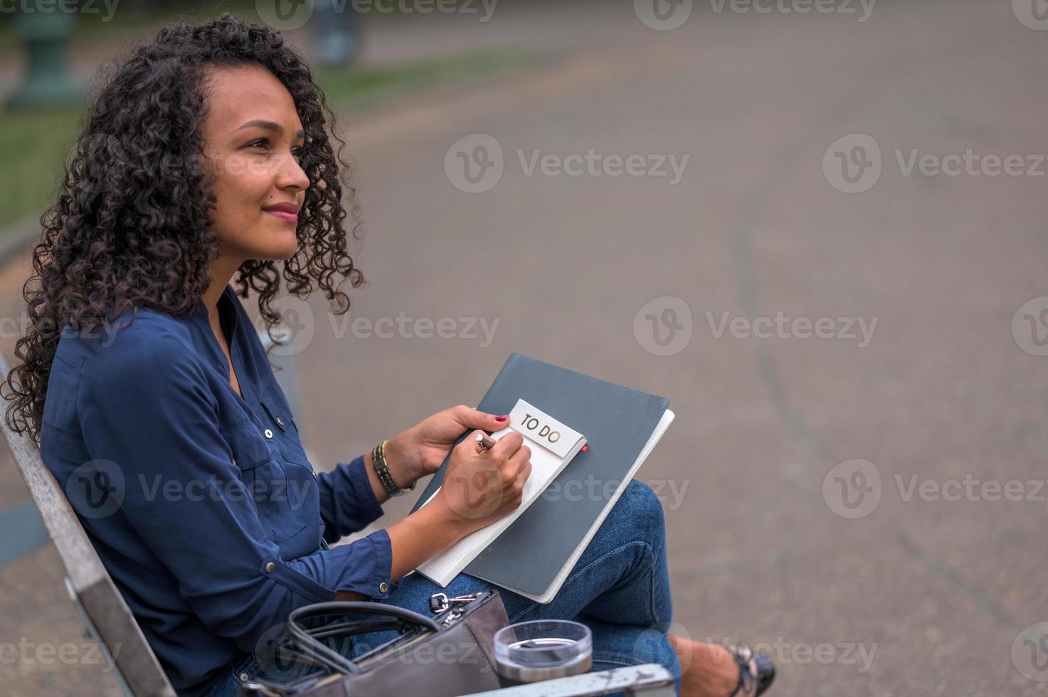 mulher negra com esmalte vermelho refletindo sua resolução de ano novo em um caderno de lista de tarefas com uma caneta preta foto