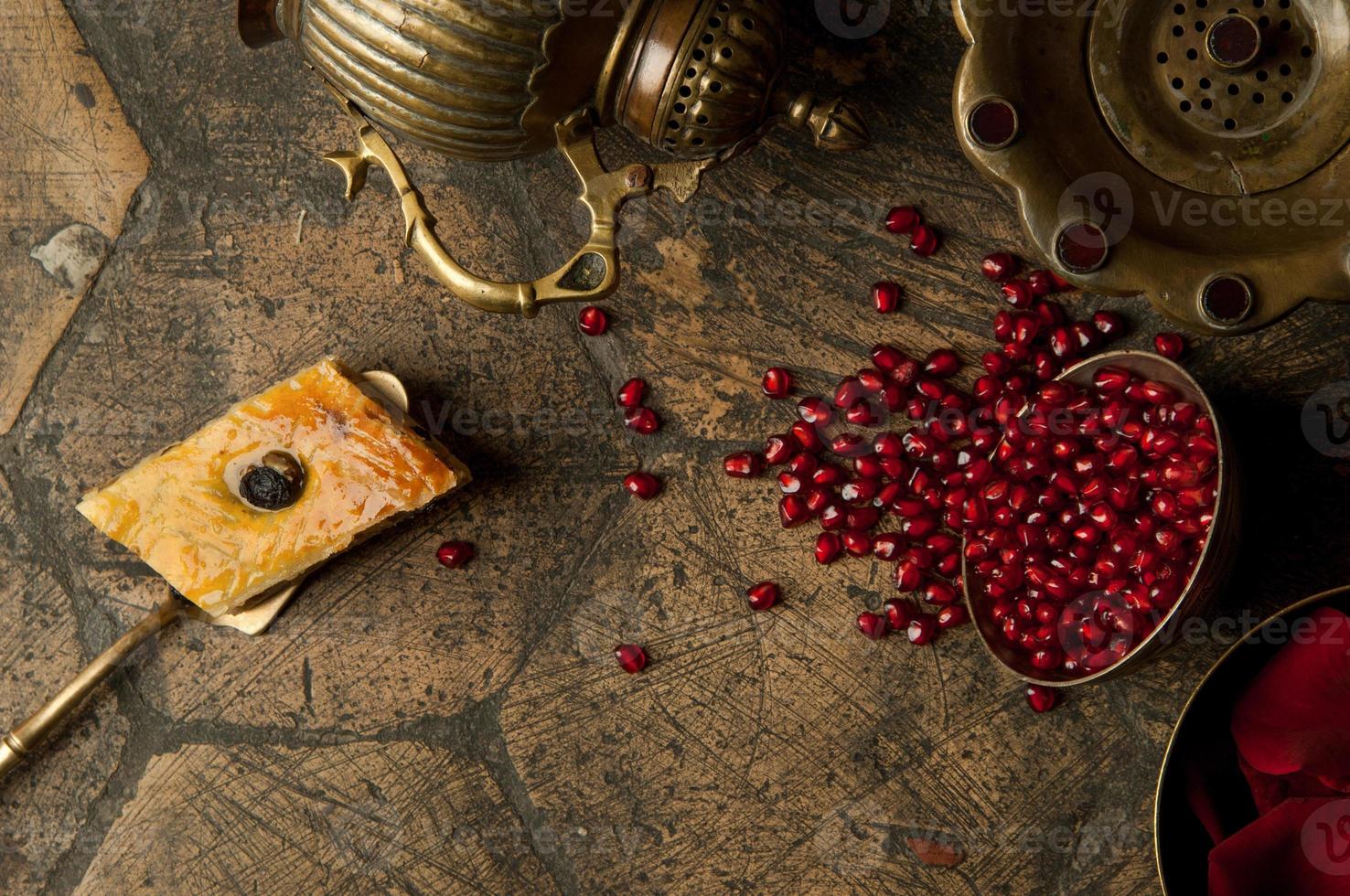 grãos e sementes de romã com um jarro de cobre em uma antiga pedra de pavimentação decorativa. um jarro de cobre antigo com uma romã e bolo em uma telha velha foto