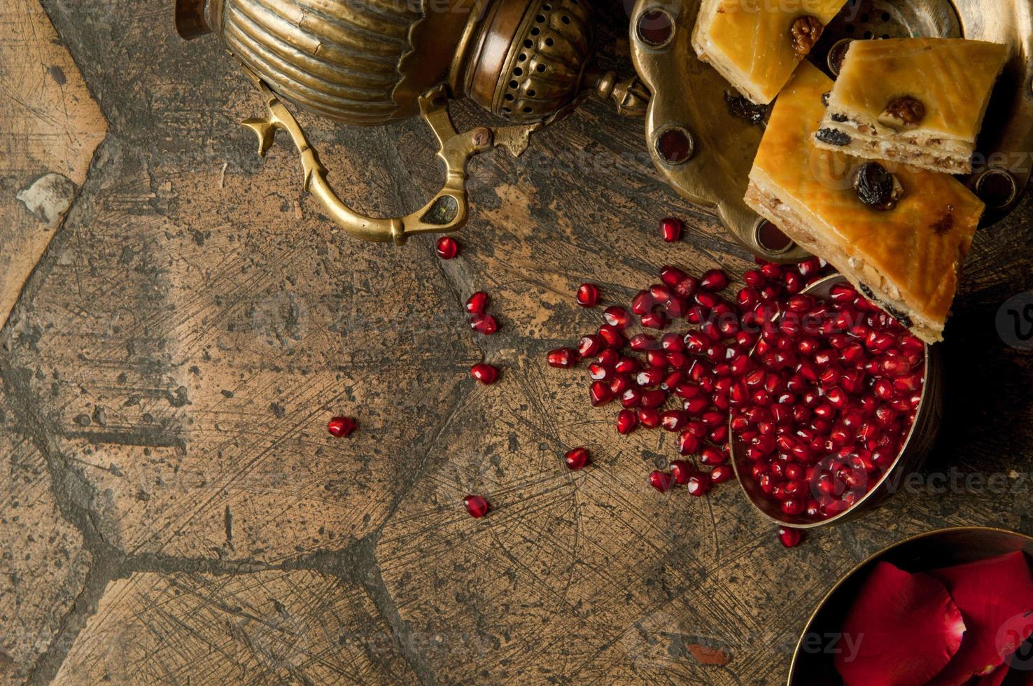 grãos e sementes de romã com um jarro de cobre em uma antiga pedra de pavimentação decorativa. um jarro de cobre antigo com uma romã e bolo em uma telha velha foto