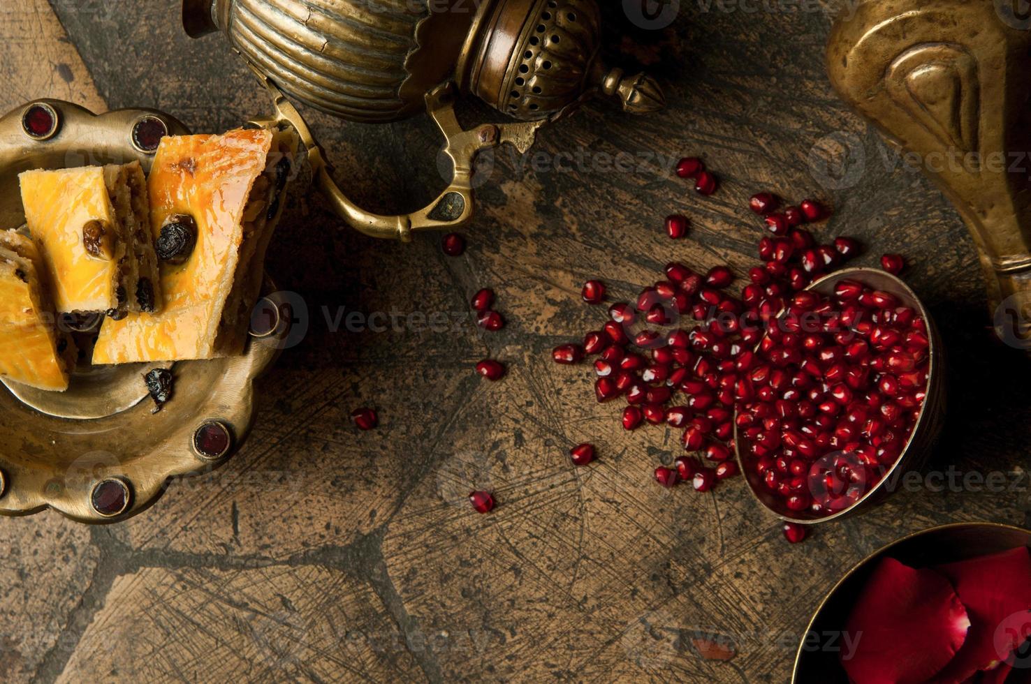 grãos e sementes de romã com um jarro de cobre em uma antiga pedra de pavimentação decorativa. um jarro de cobre antigo com uma romã e bolo em uma telha velha foto