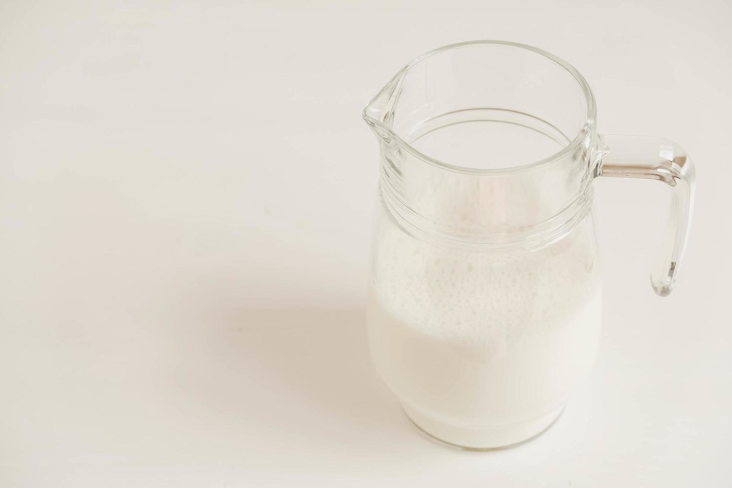 jarro de vidro com leite em uma mesa branca foto