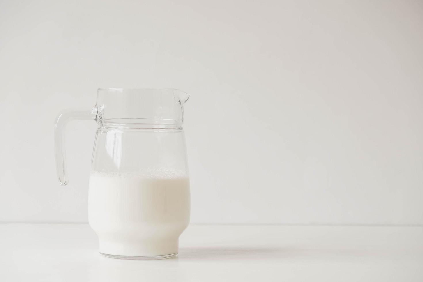 jarro de vidro com leite em uma mesa branca foto