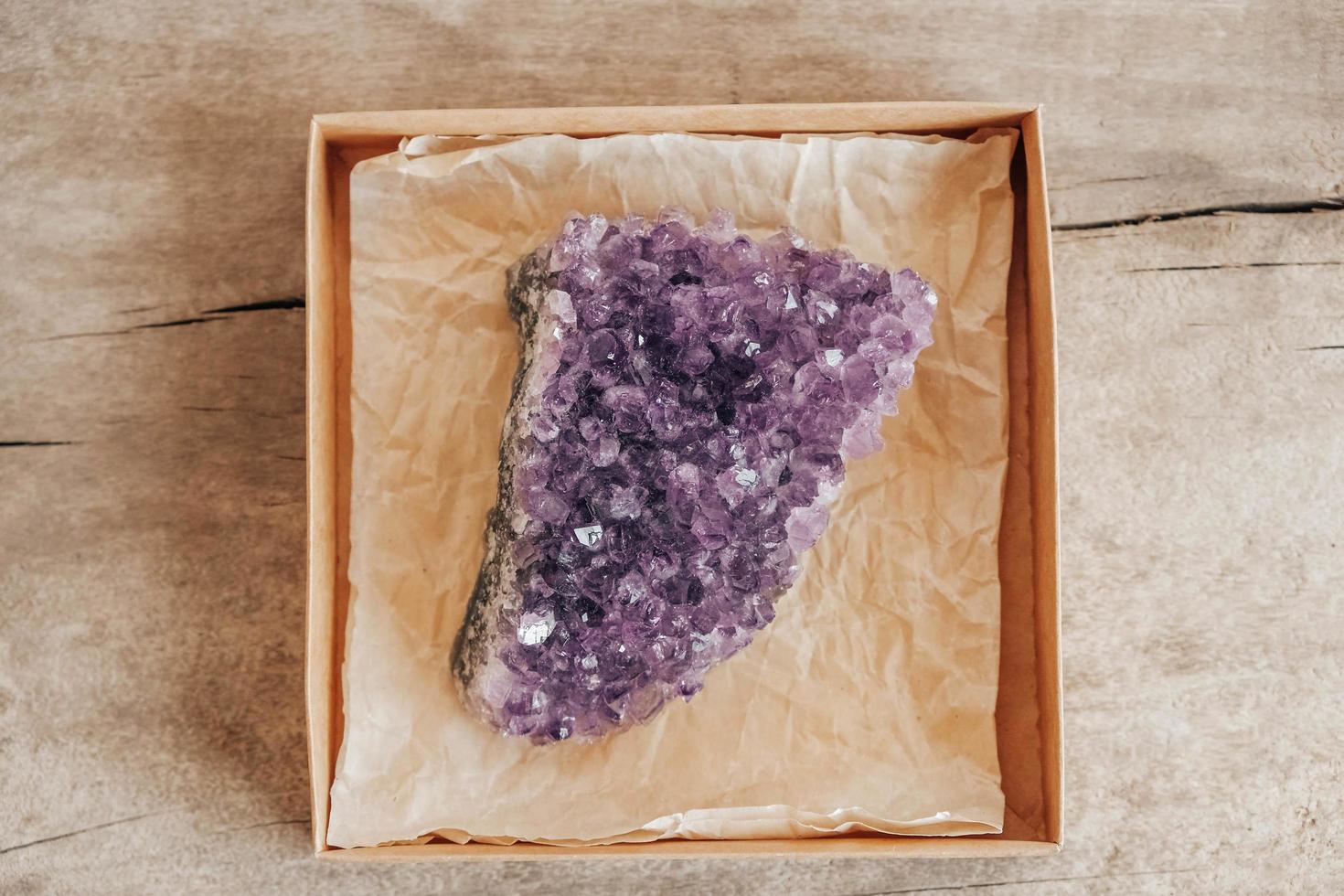 cristal de ametista violeta em uma caixa de papel kraft em fundo de madeira foto