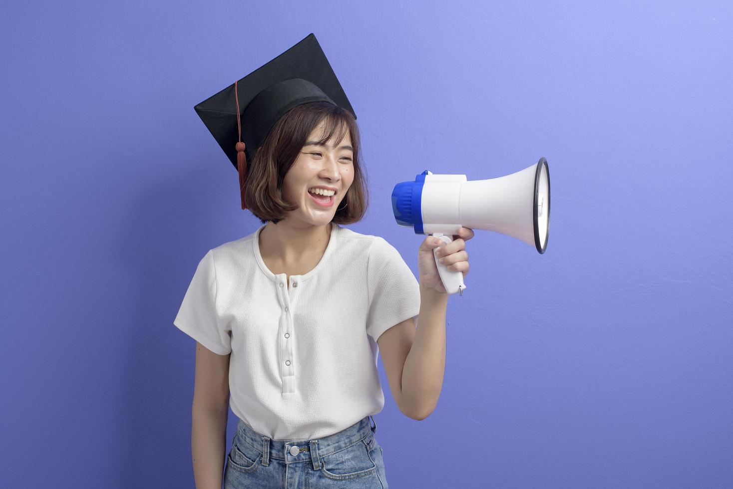 retrato de estudante asiático graduado segurando megafone isolado estúdio de fundo roxo foto