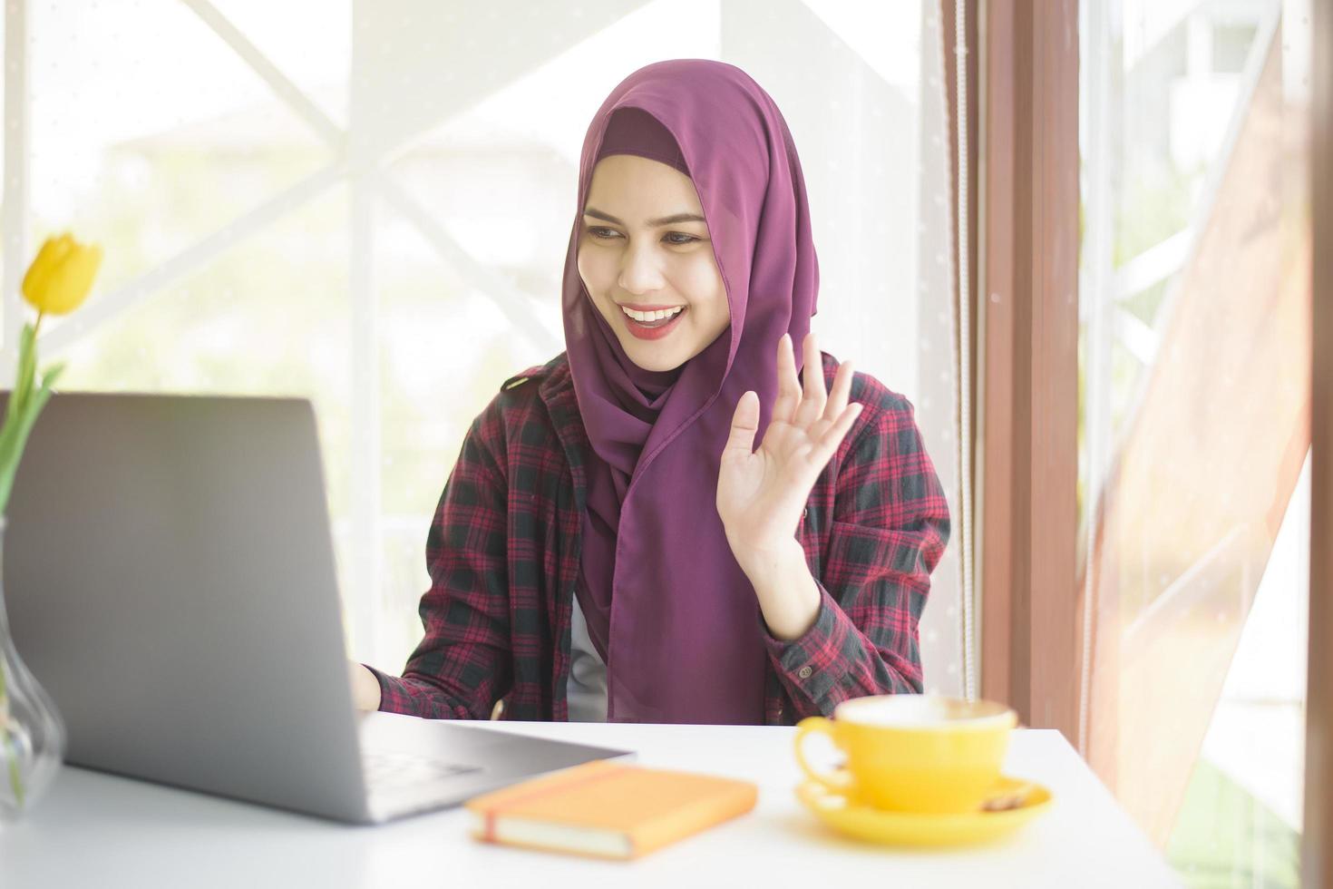 mulher muçulmana com hijab está trabalhando com computador portátil na cafeteria foto