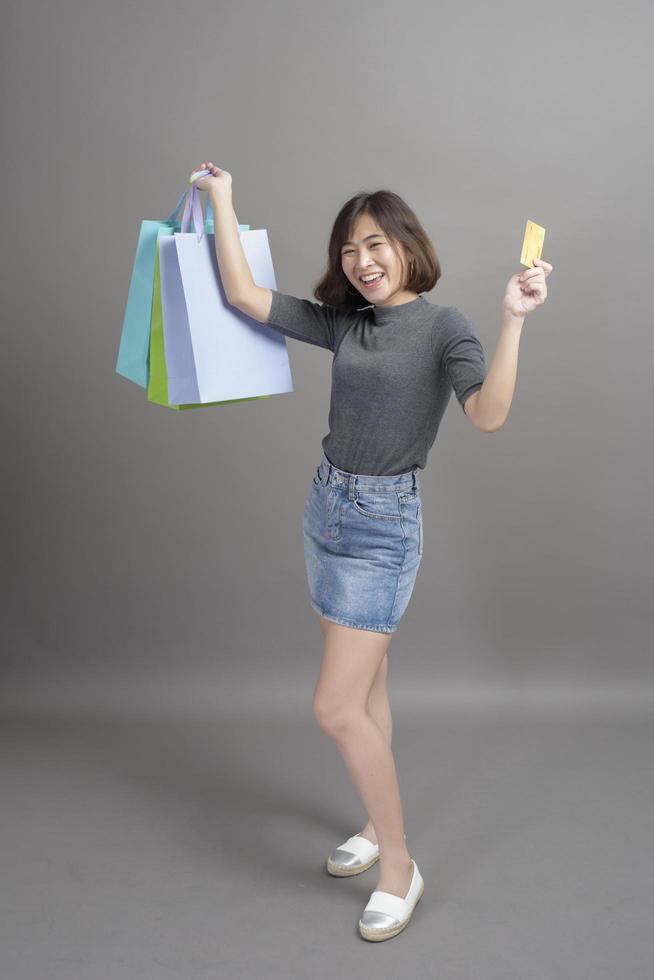 retrato de uma jovem linda mulher asiática segurando o cartão de crédito e a sacola colorida isolada sobre o estúdio de fundo cinza foto