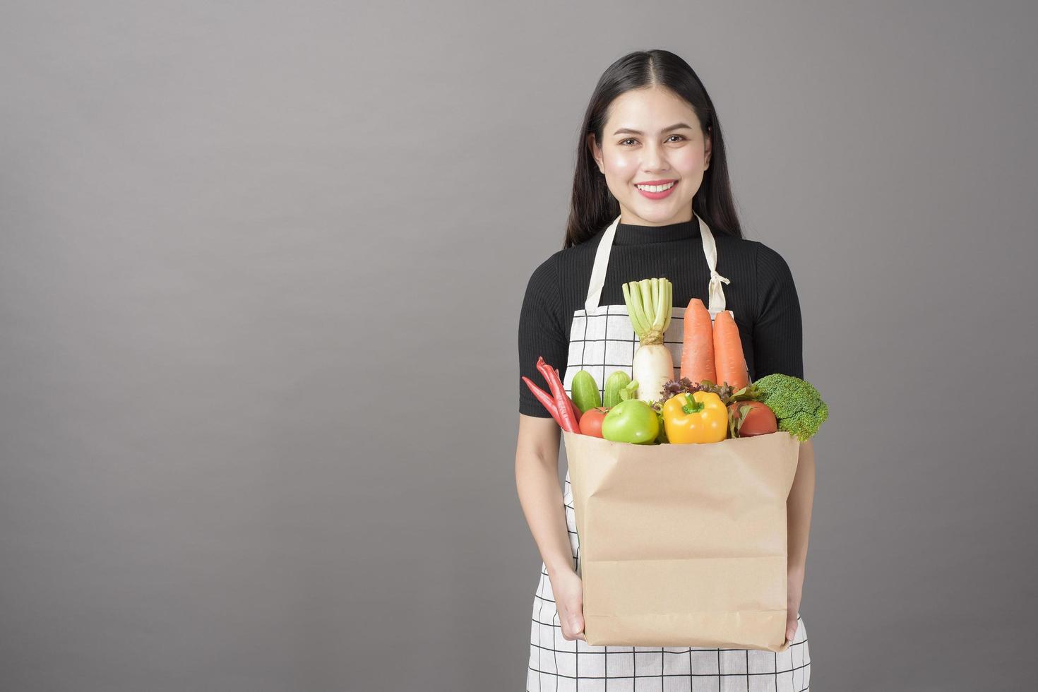 retrato de mulher jovem e bonita com legumes na sacola de compras em fundo cinza de estúdio foto