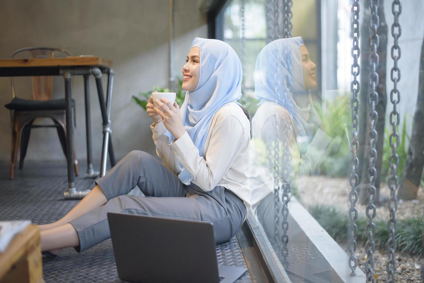 mulher muçulmana com hijab está trabalhando com computador portátil na cafeteria foto