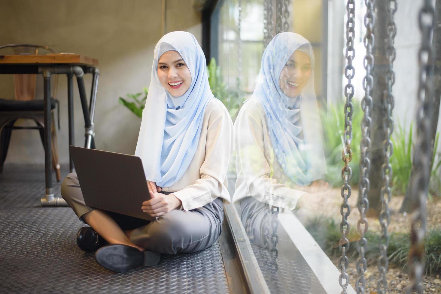 mulher muçulmana com hijab está trabalhando com computador portátil na cafeteria foto