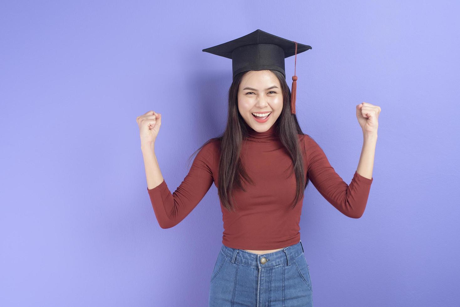 retrato de mulher jovem estudante universitário com chapéu de formatura em fundo violeta foto