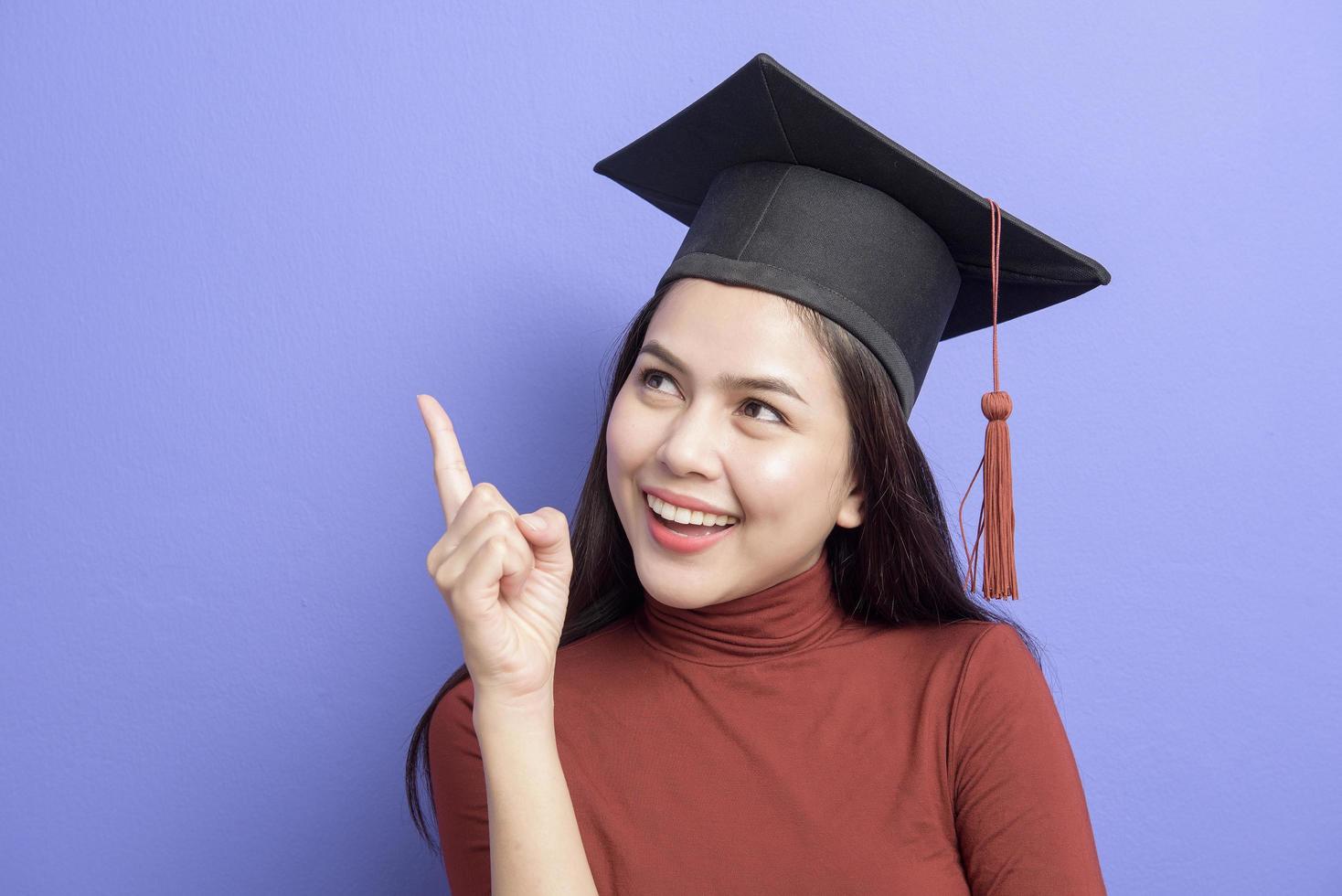 retrato de mulher jovem estudante universitário com chapéu de formatura em fundo violeta foto