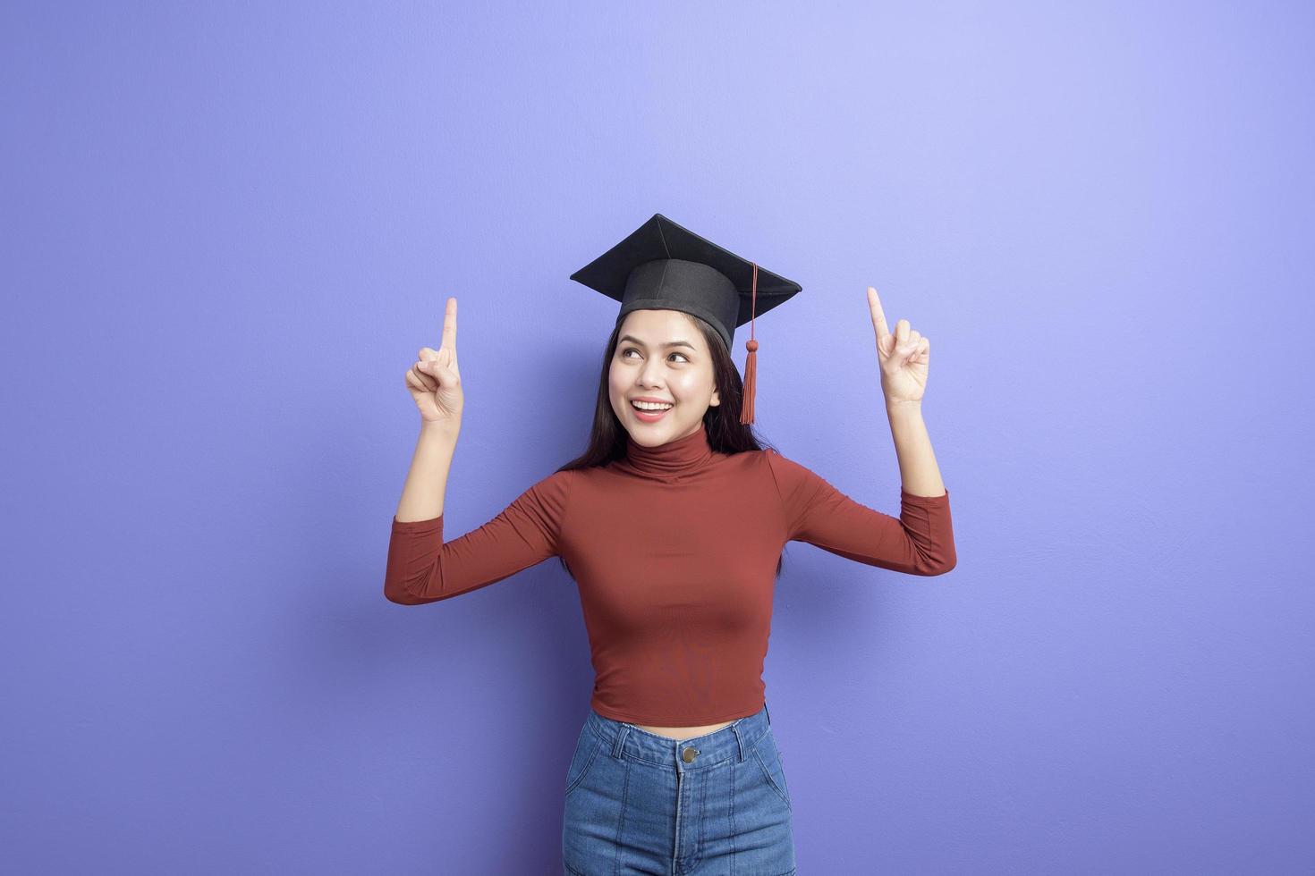 retrato de mulher jovem estudante universitário com chapéu de formatura em fundo violeta foto