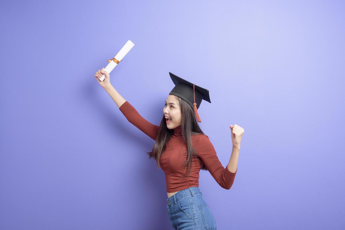 retrato de mulher jovem estudante universitário com chapéu de formatura em fundo violeta foto