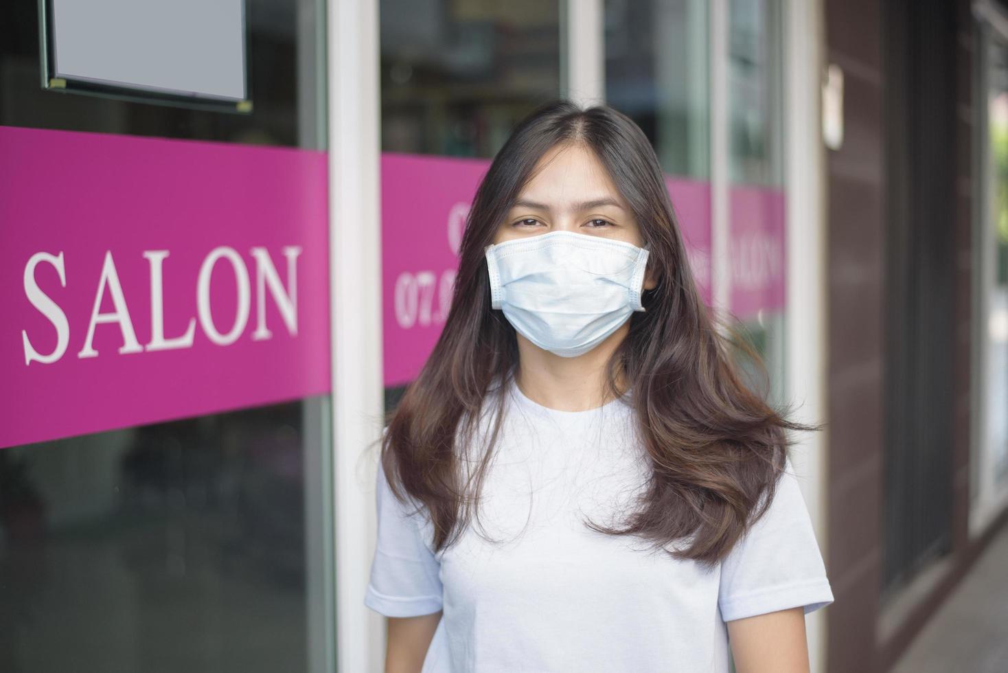 uma jovem está usando máscara facial para proteção covid-19 em frente à loja de salão, conceito de segurança do salão foto