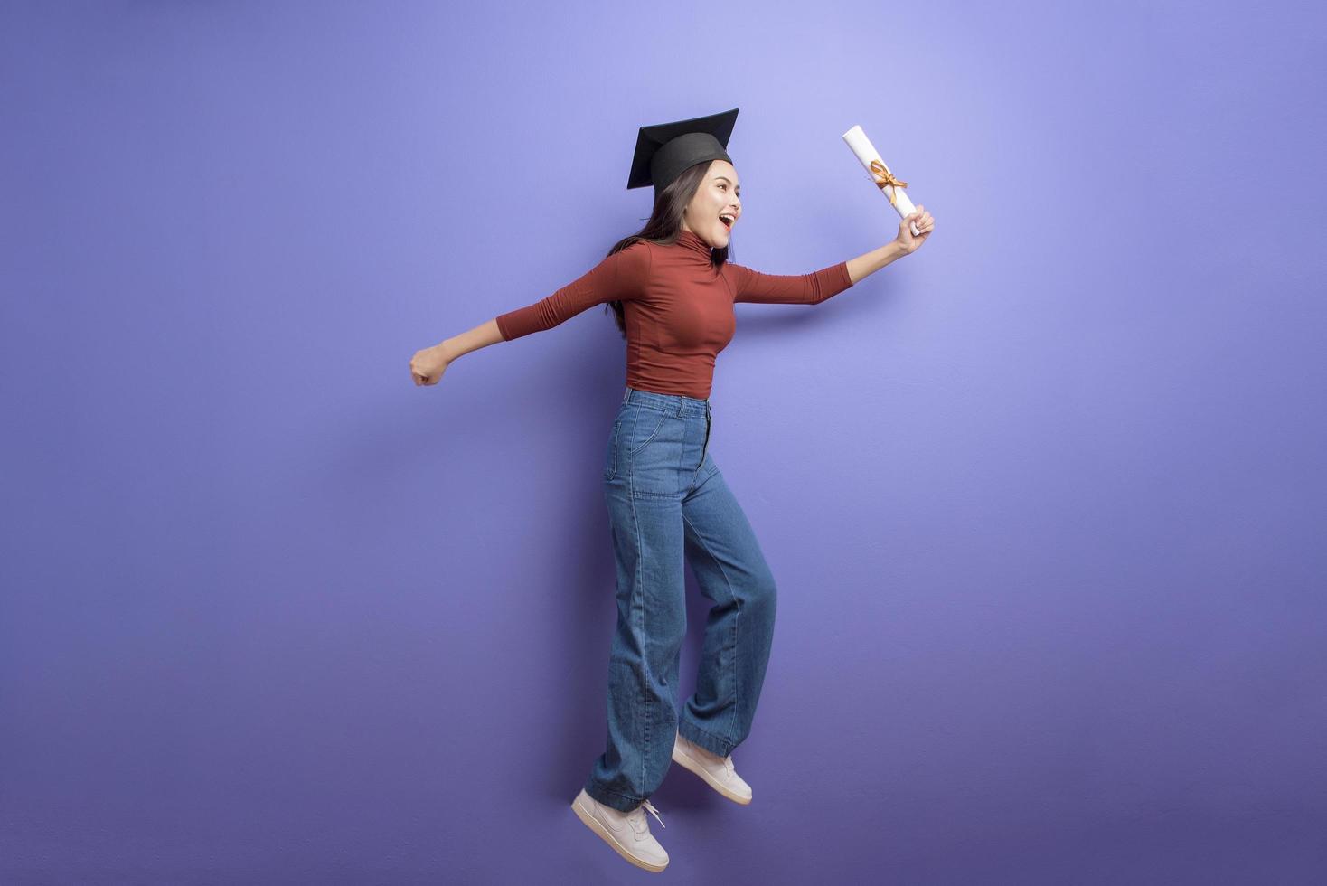 retrato de mulher jovem estudante universitário com chapéu de formatura em fundo violeta foto