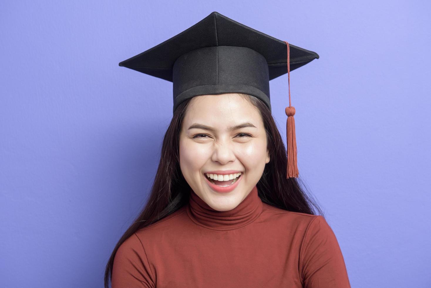 retrato de mulher jovem estudante universitário com chapéu de formatura em fundo violeta foto