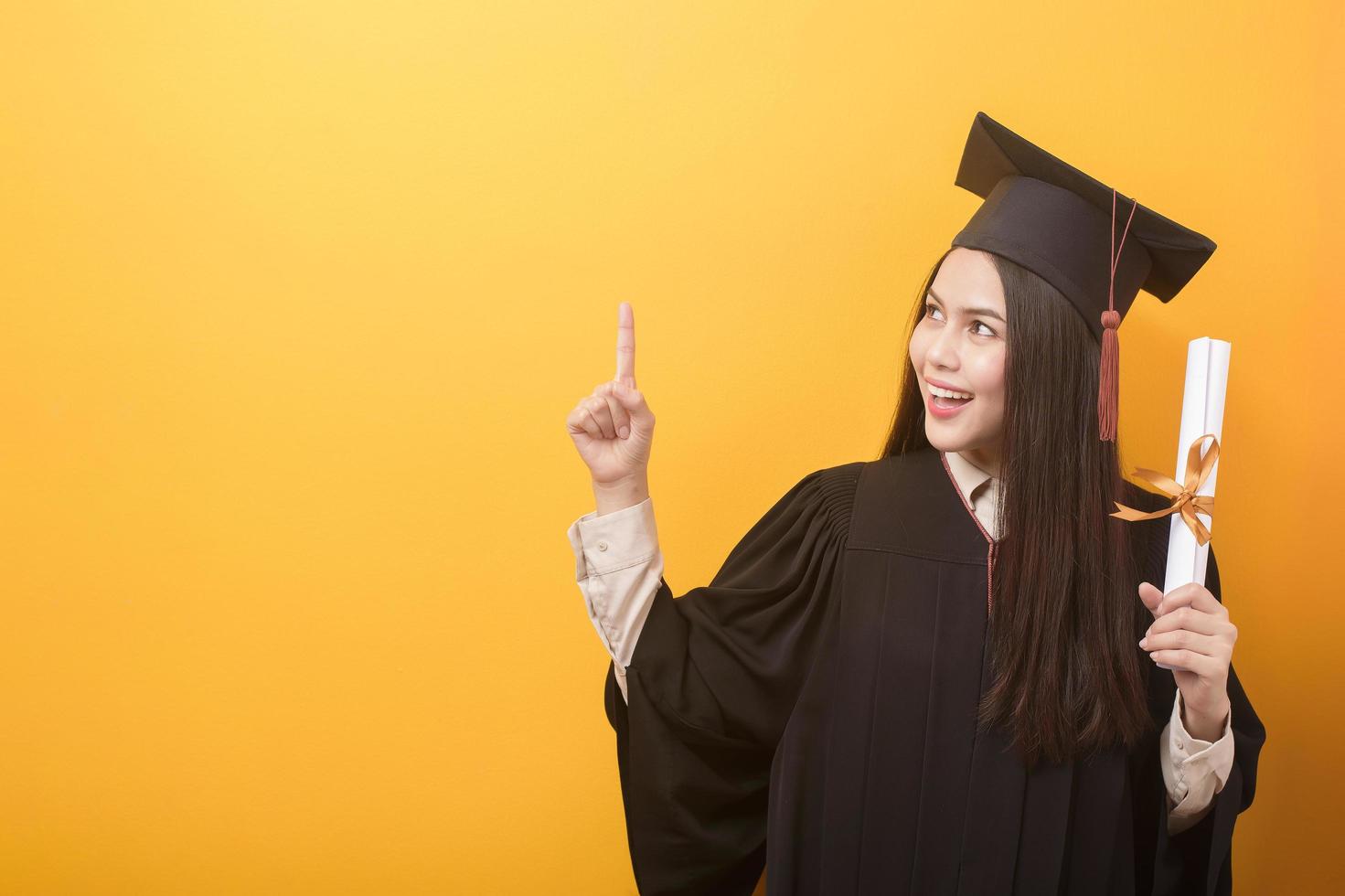 retrato de mulher bonita feliz no vestido de formatura está segurando o certificado de educação em fundo amarelo foto