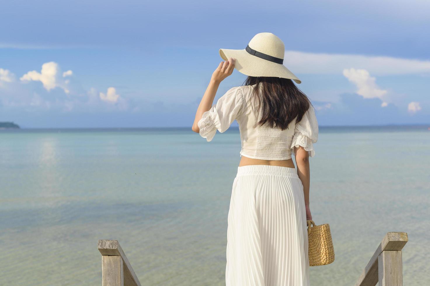 uma mulher bonita feliz no vestido branco, desfrutando e relaxando no conceito de praia, verão e férias foto
