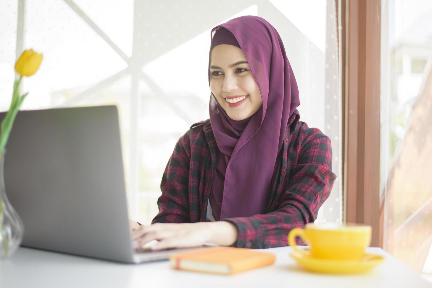 mulher muçulmana com hijab está trabalhando com computador portátil na cafeteria foto