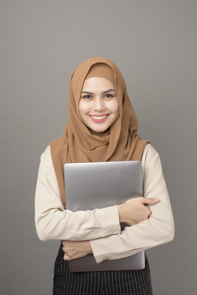retrato de mulher bonita com hijab está segurando o laptop do computador em fundo cinza foto
