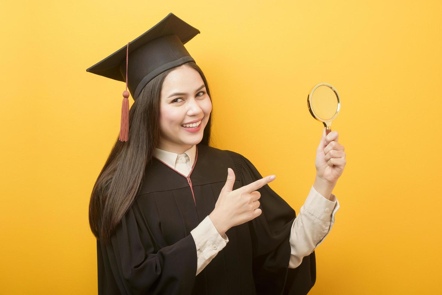 retrato de mulher bonita no vestido de formatura está segurando a lupa no fundo amarelo foto