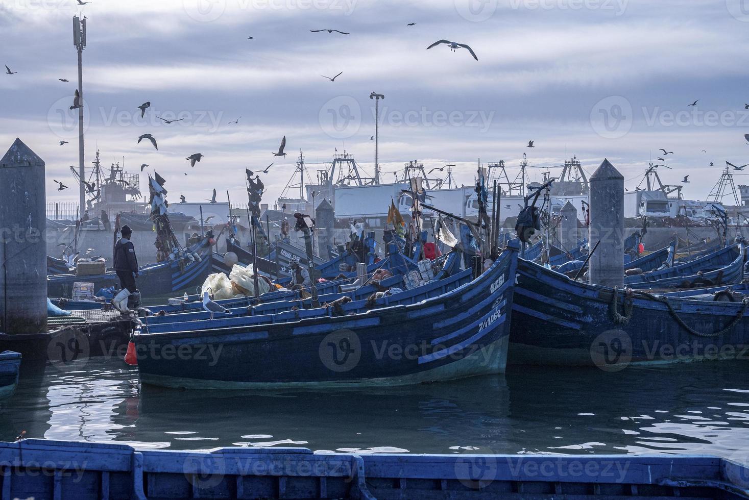 barcos de pesca azuis de madeira ancorados na marina contra o céu nublado foto