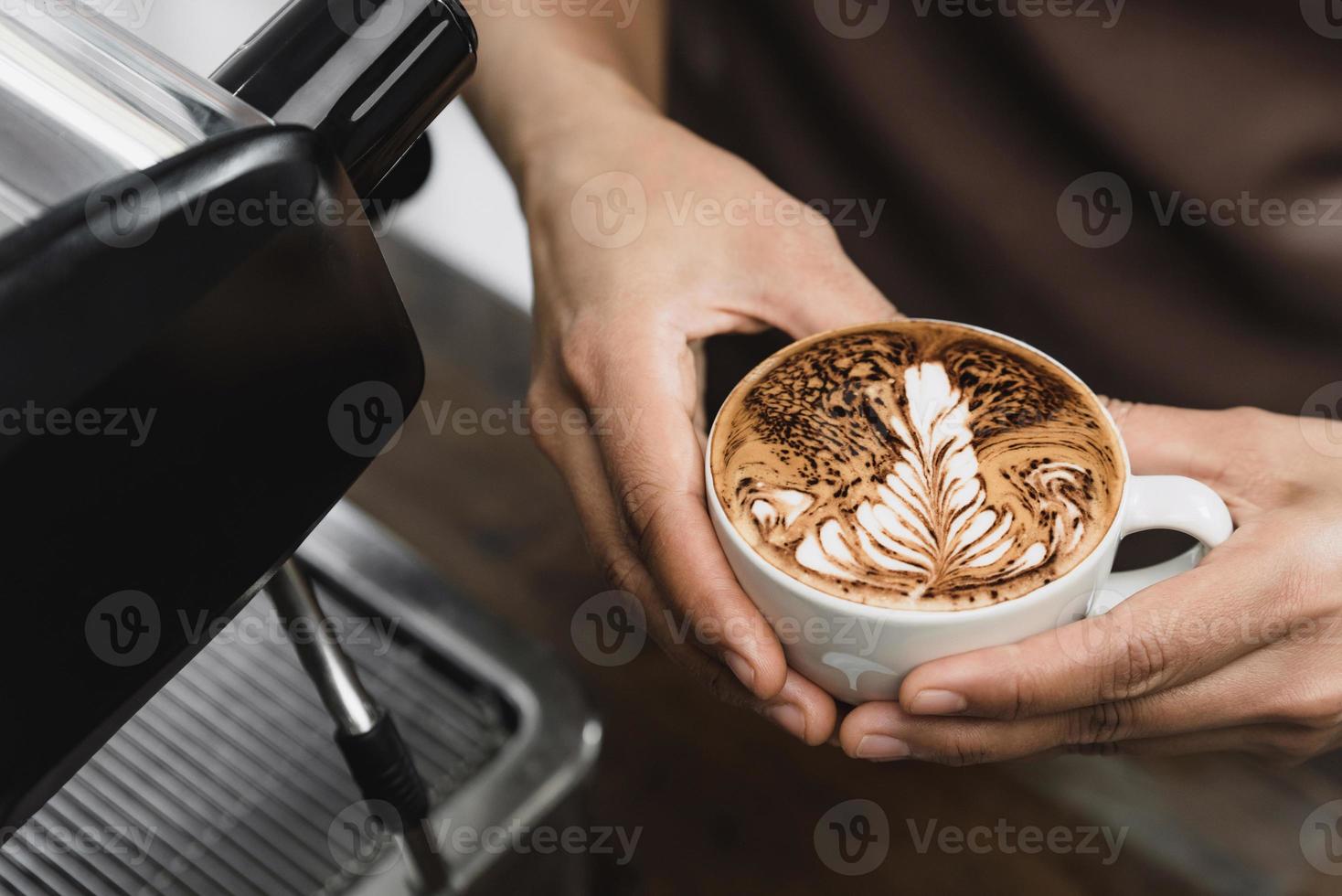 mãos de barista segurando uma xícara de café com leite prestes a servir no café foto