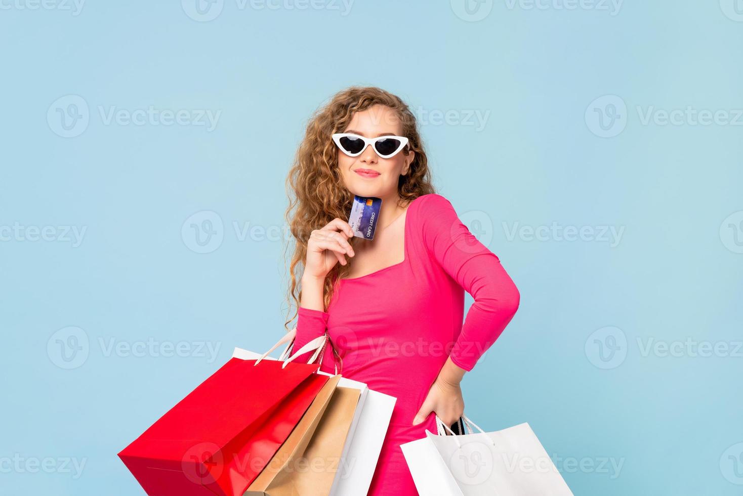 feliz linda mulher caucasiana sorridente com sacolas de compras, mostrando o cartão de crédito na mão isolado no fundo azul foto