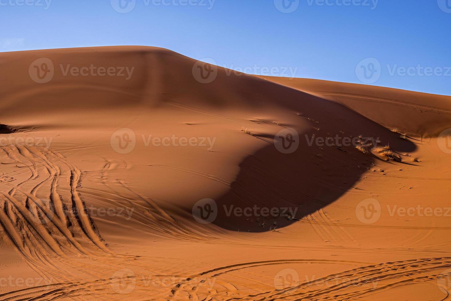 dunas de areia com marcas de pneus no deserto em dia ensolarado de verão contra o céu foto