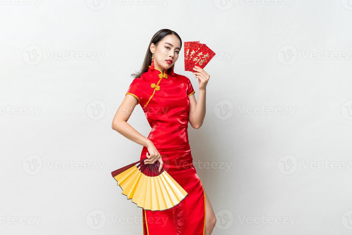 mulher asiática em traje oriental cheongsam segurando envelopes vermelhos ou ang pao e ventilador em fundo de estúdio cinza claro para conceitos de ano novo chinês, texto significa grande sorte grande lucro foto