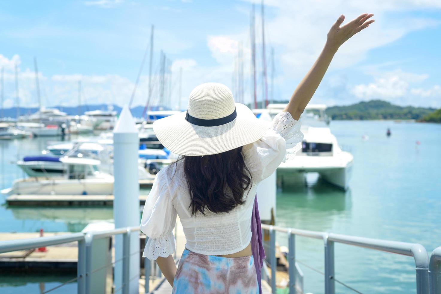 turista animado de chapéu branco desfrutando e de pé no cais com iates de luxo durante o verão foto