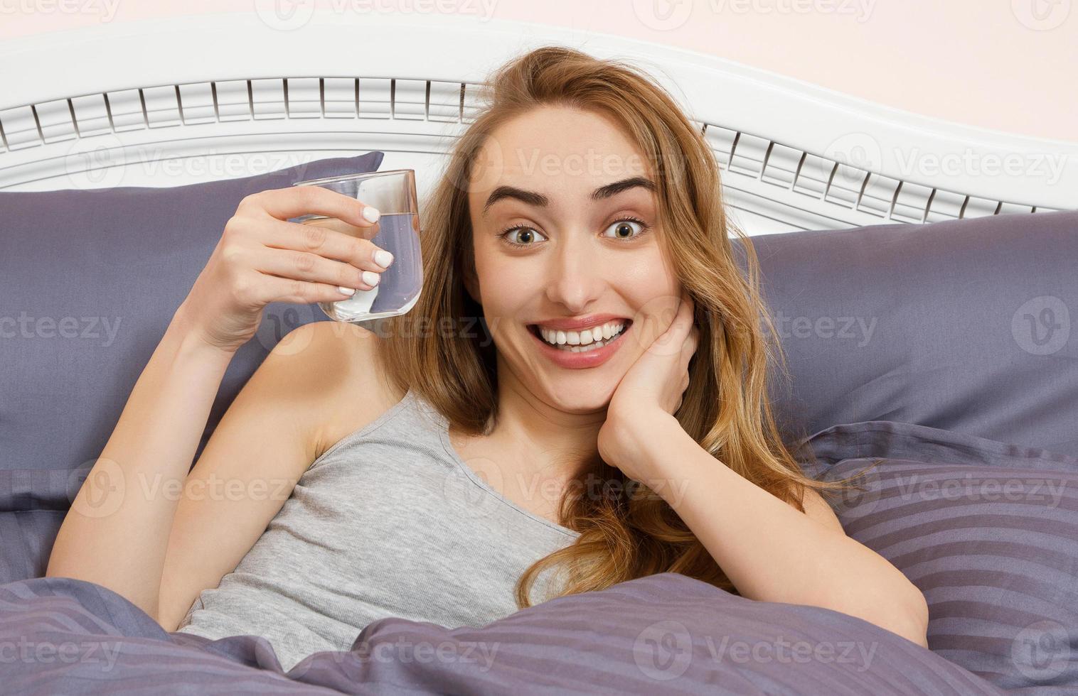 mulher emocional feliz bebe um copo de água no quarto de manhã foto