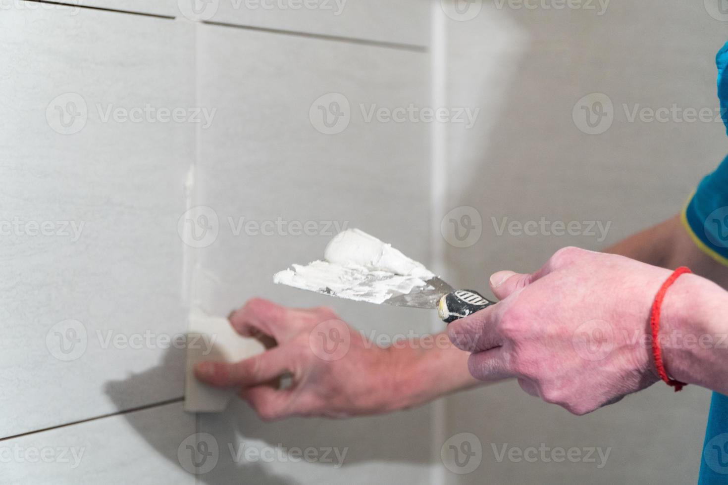 trabalhador com uma espátula de borracha preencha as costuras com uma solução. obras de acabamento. a tecnologia de colocação de azulejos foto