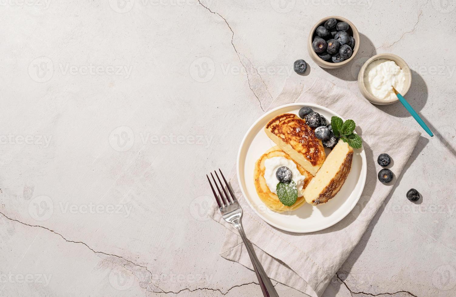 panquecas de queijo cottage servidas com requeijão e mirtilos, vista superior plana sobre fundo de concreto, copie o espaço foto