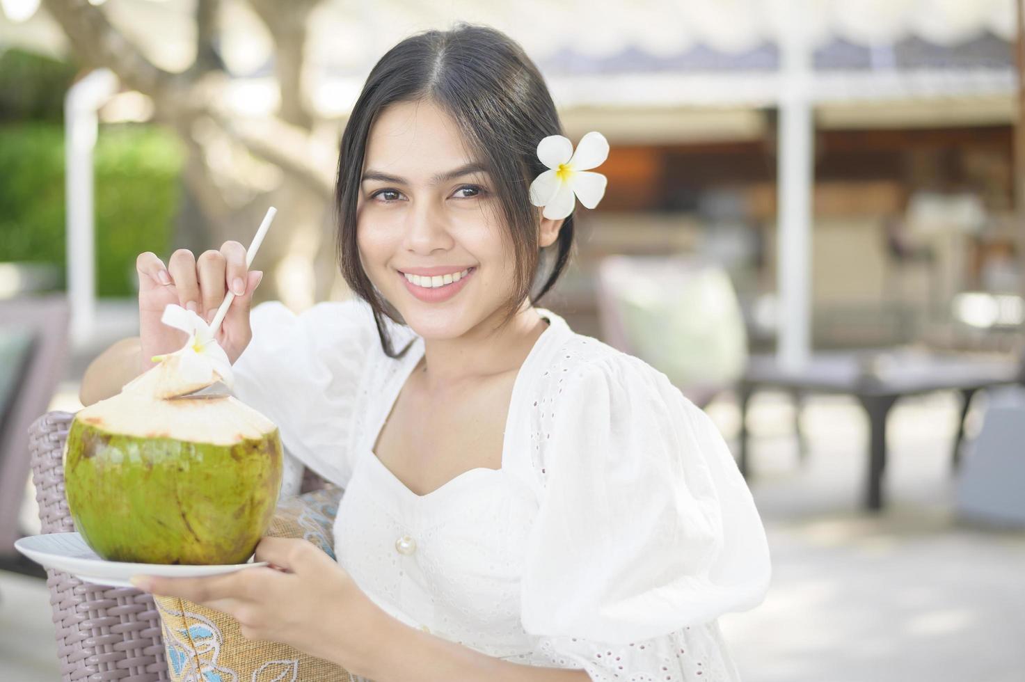 turista de mulher bonita com flor branca no cabelo bebendo coco sentado na espreguiçadeira durante as férias de verão foto