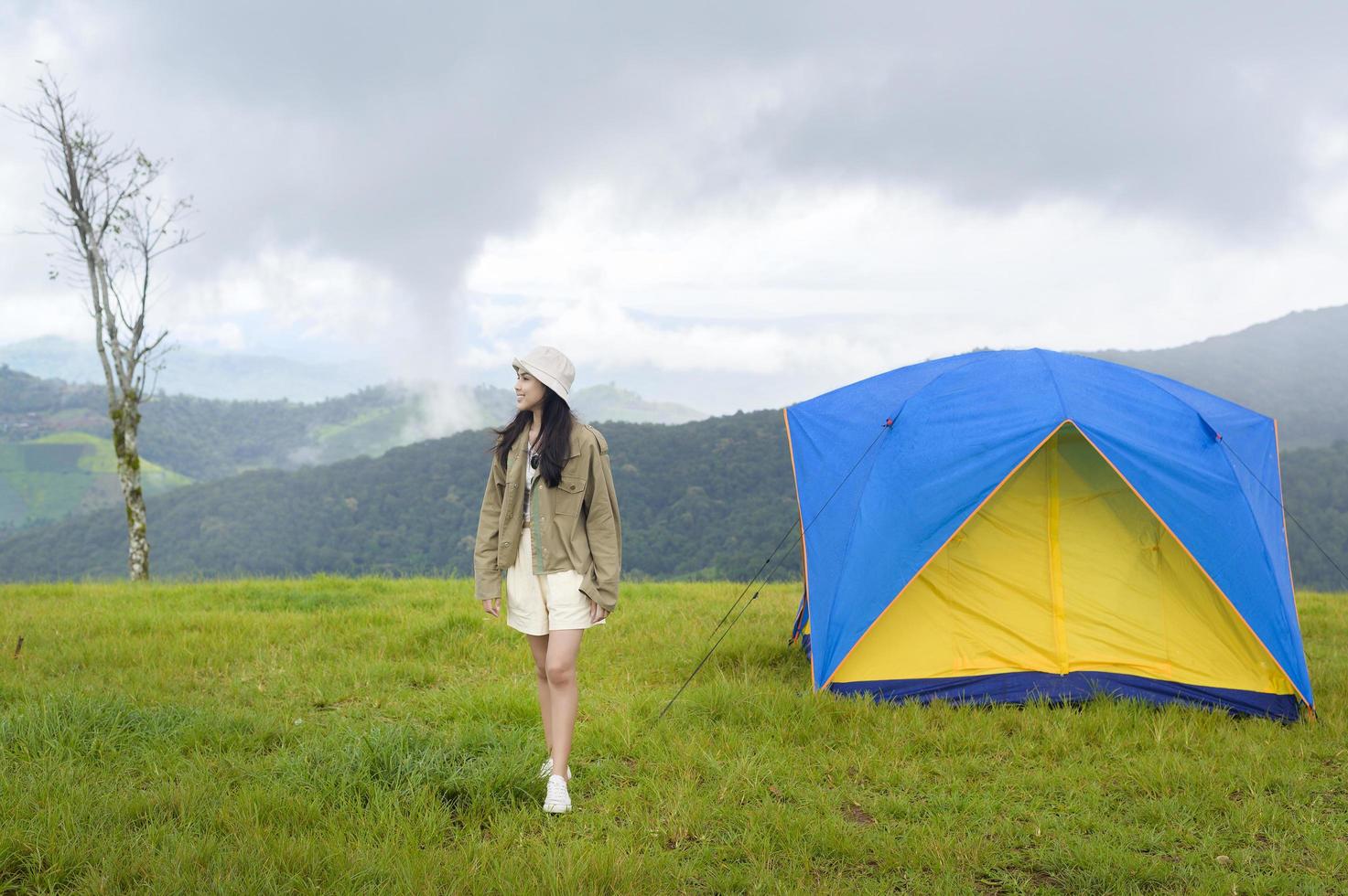 mulher viajando feliz desfrutando e relaxando perto da barraca de acampamento sobre a bela montanha verde na estação chuvosa, clima tropical. foto