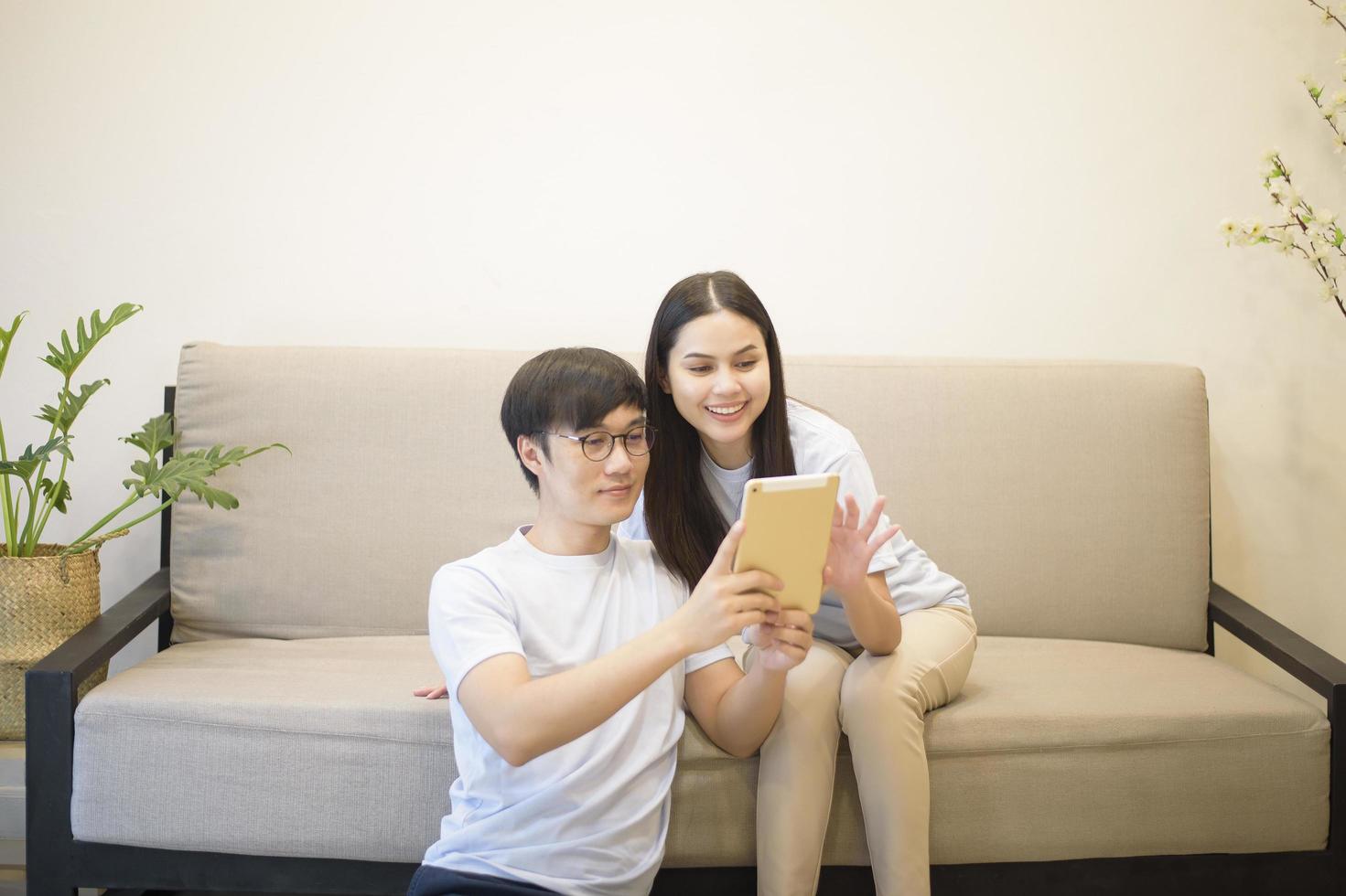 um casal feliz vestindo camisa azul está relaxando e segurando um tablet em um sofá em casa foto