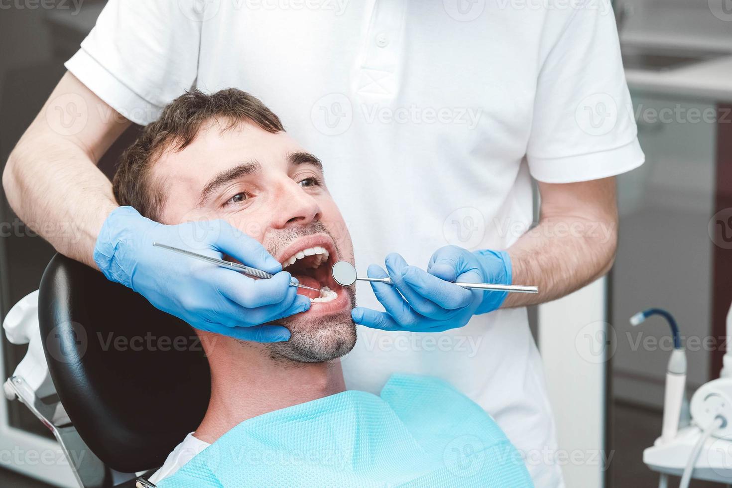 dentista examina os dentes de um paciente do sexo masculino na cadeira do dentista foto