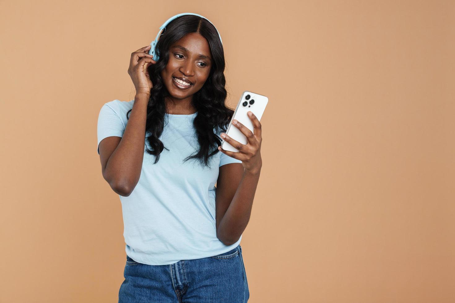 mulher africana sorridente, mensagens de texto por telefone com fones de ouvido foto