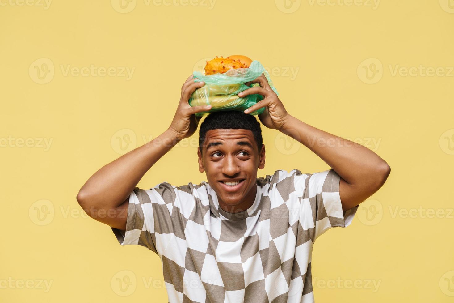 homem africano positivo segurando frutas em saco de lixo plástico na cabeça foto