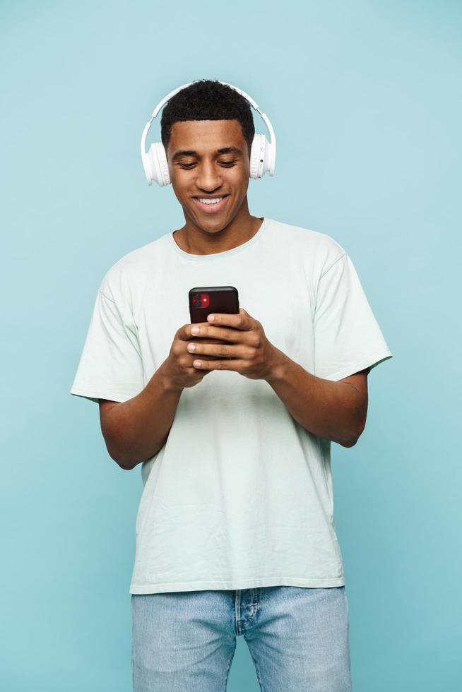 homem africano positivo digitando por telefone com fones de ouvido foto