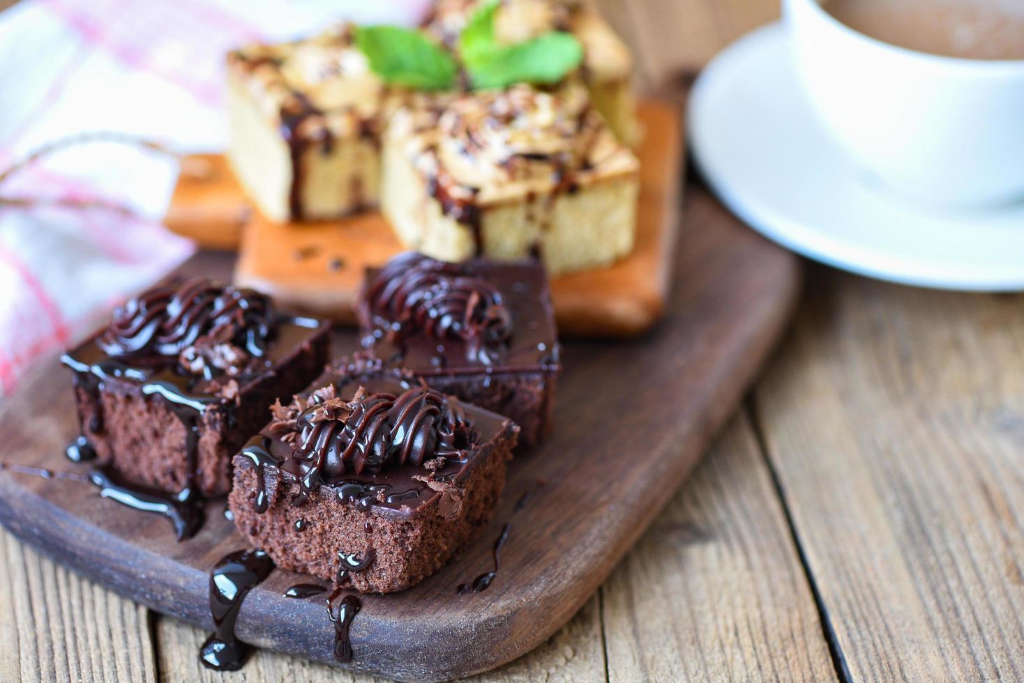 bolo de café deliciosa sobremesa servida na mesa - fatia de bolo de chocolate no fundo da placa de madeira com folha de hortelã e xícara de café no café da manhã foto