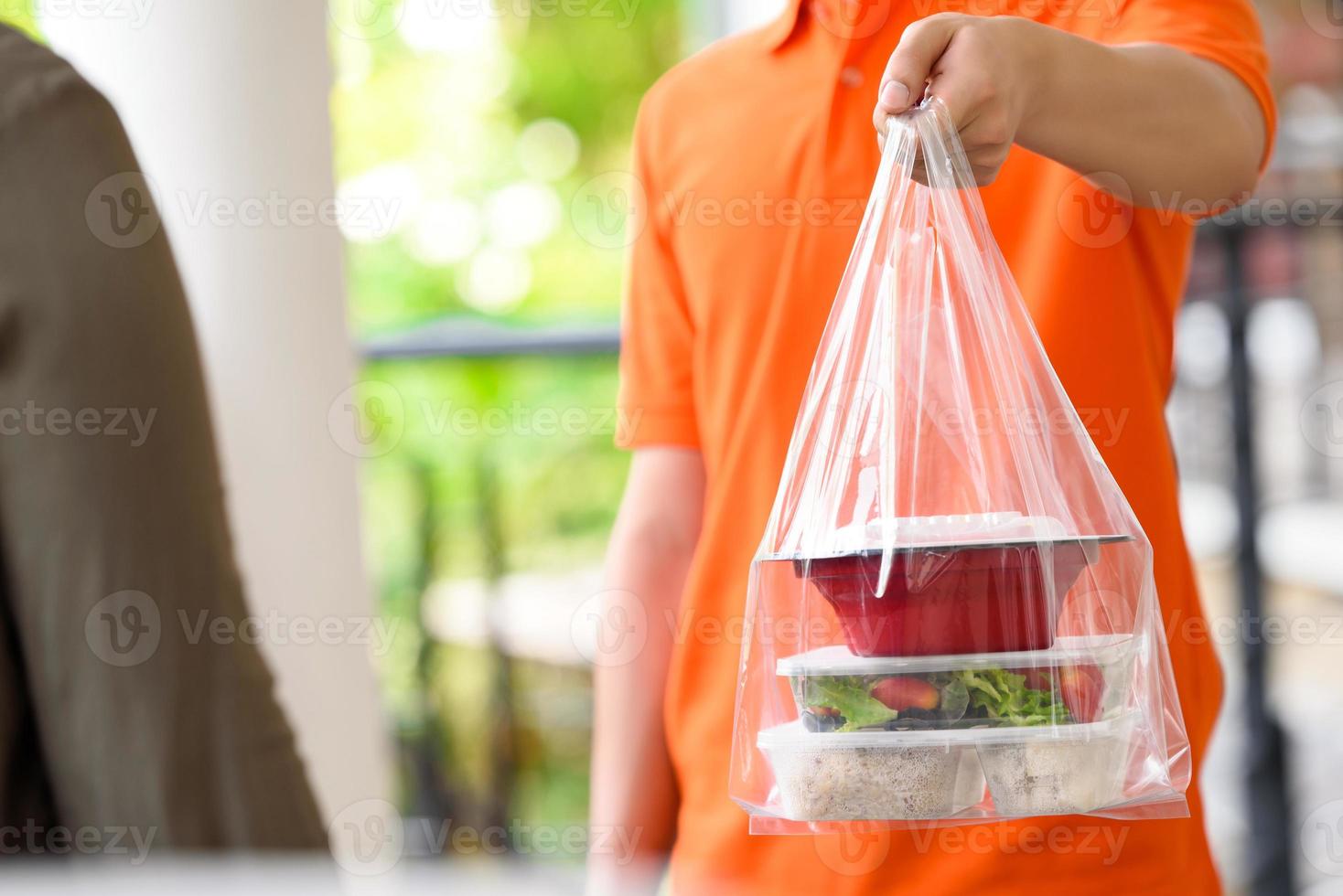 entregador de uniforme laranja entregando comida asiática em caixas para viagem ao cliente em casa foto