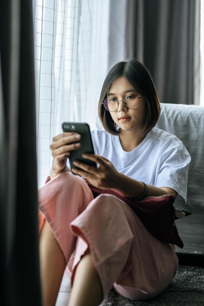 uma mulher vestindo uma camisa branca, sentada na cama e jogando um smartphone. foto