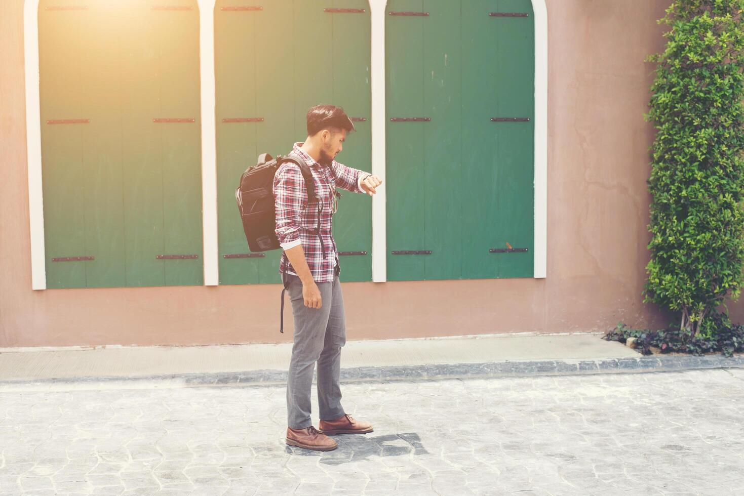 jovem olhando para o relógio de mão antes de viajar com a mochila no ombro. foto