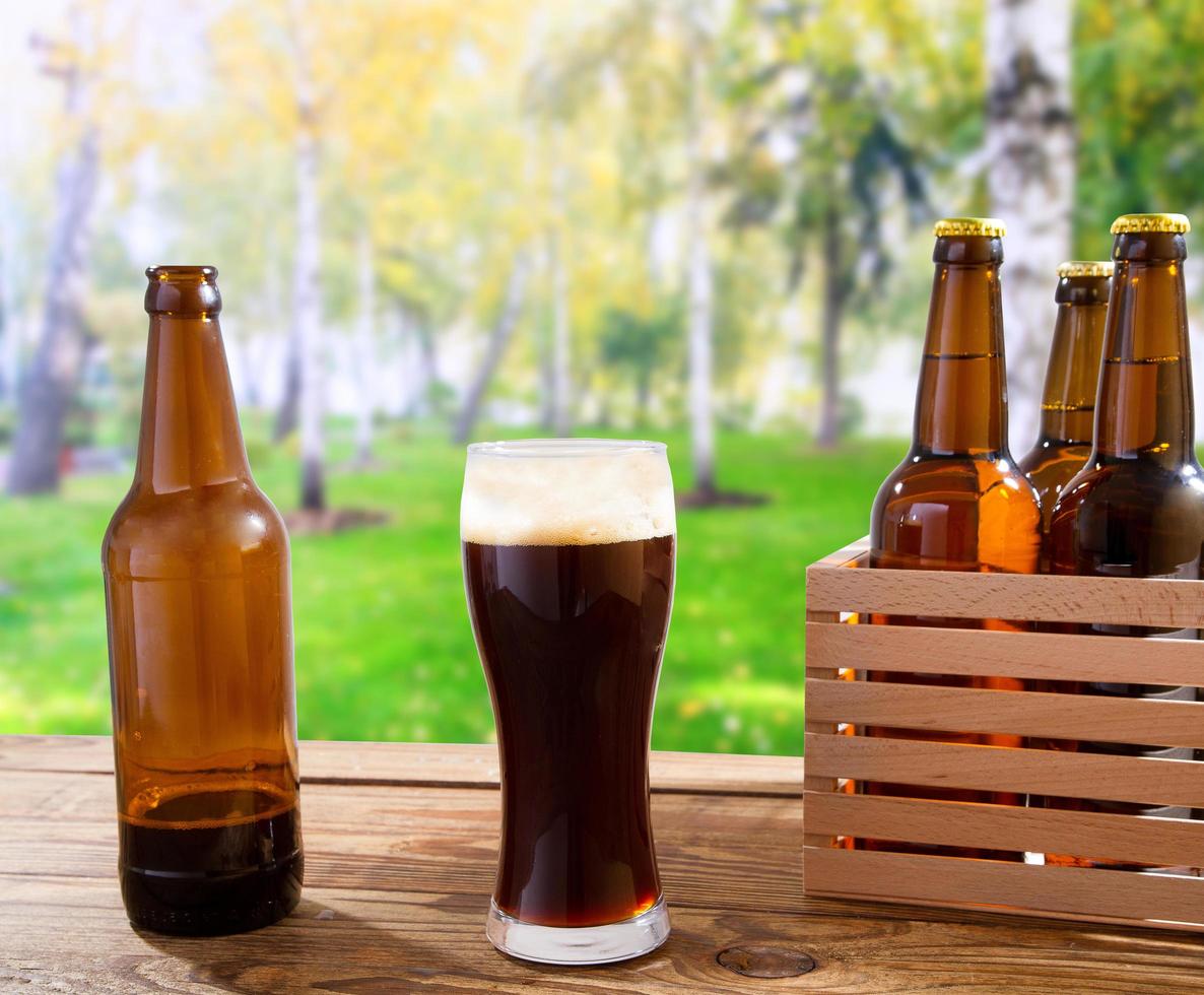 cerveja em vidro, garrafas na mesa de madeira com parque da cidade turva no fundo, conceito de comida e bebida, espaço de cópia, foco seletivo foto